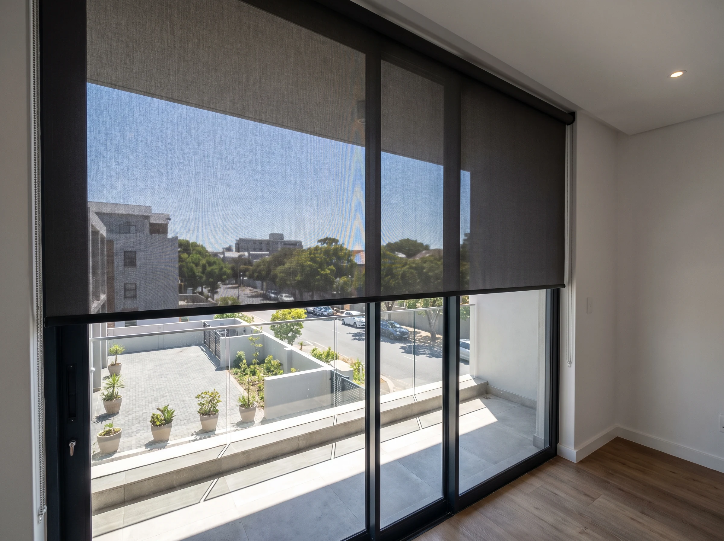 Motorised sunscreen roller blind half drawn across a full-height sliding door on a Claremont, Cape Town apartment balcony